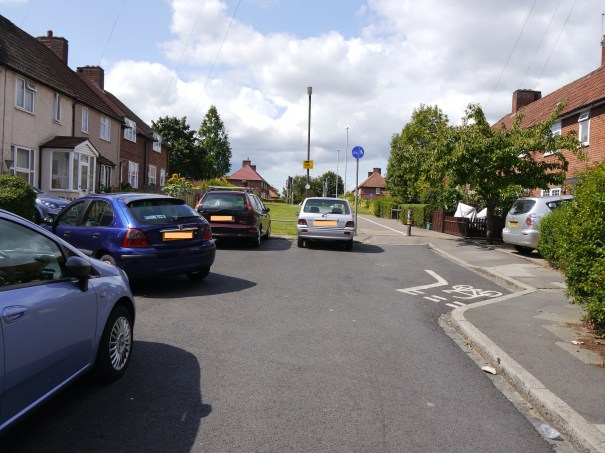 A photo showing the interface between the trafficked street and the cycle path/footway at Leominster Walk, looking west towards St Helier Avenue